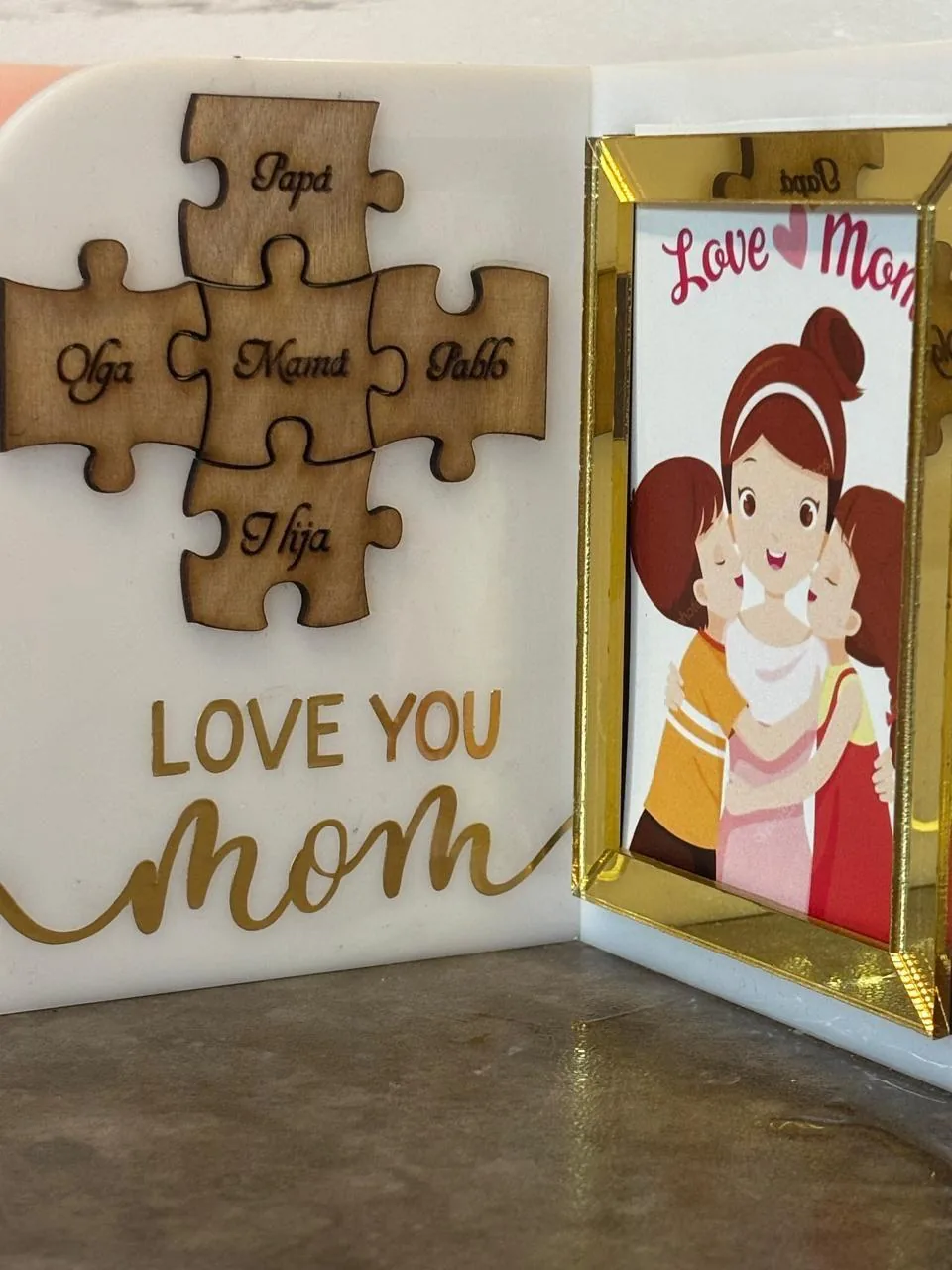 Cuadro personalizado del Día de las Madres en acrílico blanco con piezas de rompecabezas de madera grabadas con los nombres de la familia y portarretrato en acrílico espejo dorado.