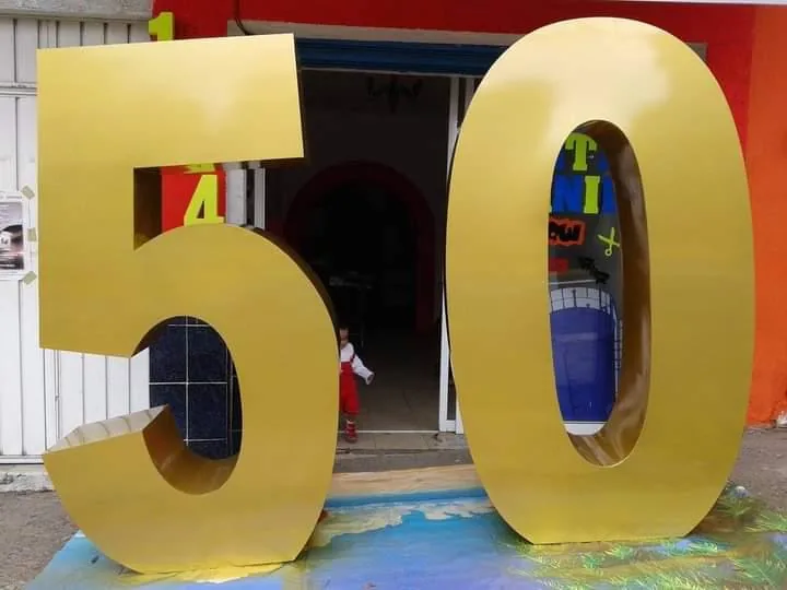 Números gigantes 50 en acabado dorado para decoración de fiesta de cumpleaños, montados a la entrada de un local.