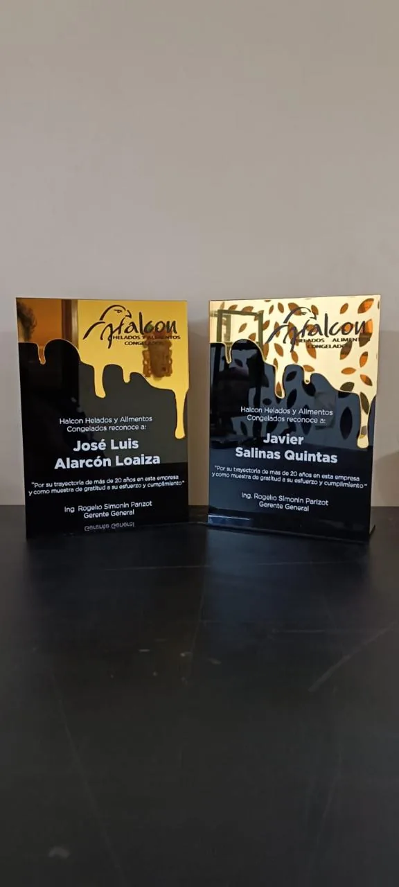 Par de placas de reconocimiento en acrílico espejo dorado y negro grabadas para Halcón Helados y Alimentos Congelados, con nombre del homenajeado y texto conmemorativo.